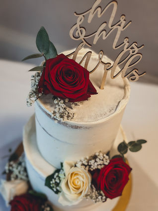 Large two tier semi-naked wedding cake with red and ivory roses and gypsophila, on a gold stand at Alexandra House. Flowers by Ivory Rose Florist.