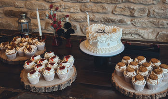 “Elegant Halloween wedding dessert table with a vintage heart-shaped cake reading ‘til death’, surrounded by cupcakes on wooden log stands at Winkworth Farm.”