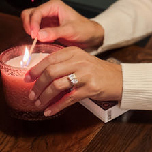 Woman wearing the Tate pear and emerald-cut diamond ring while lighting a candle.
