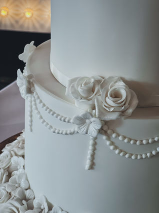 White wedding cake with piped pearls, handmade sugar roses, and a romantic topper on a silver stand at The Swan Hotel, Bibury.