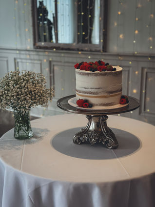 Semi-naked Biscoff cutting cake decorated with fresh strawberries, raspberries and blueberries on a silver cake stand at The Manor by the Lake.