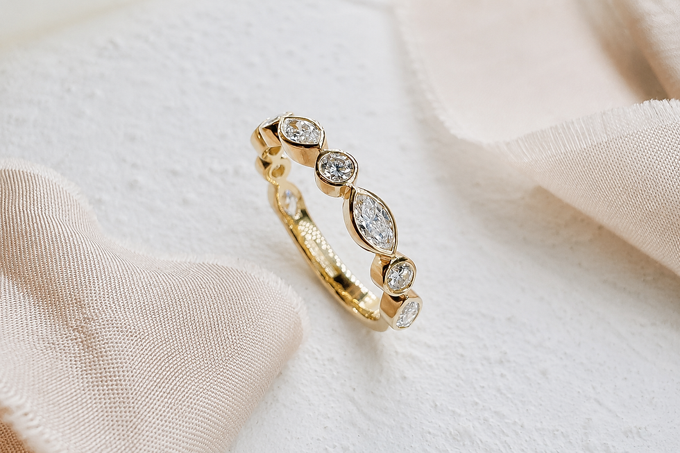 Yellow gold diamond eternity ring with marquise and round diamonds on soft neutral fabric background