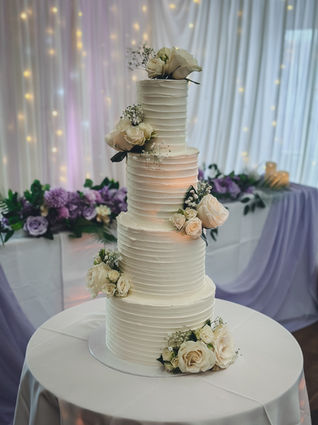 Four-tier buttercream wedding cake with ivory roses and floral accents by Purple Orchid, designed for Halina & Suman’s wedding at Supermarine Sports Club.