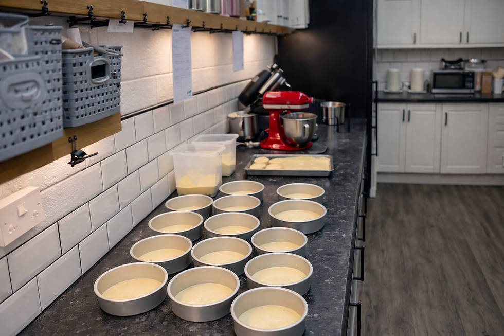 Cake batter prepared in multiple cake tins on a workbench in Kimmi’s Cakes studio kitchen in Swindon, ready for baking.