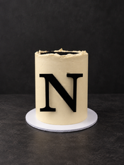 Tall minimalist birthday cake in ivory ganache with a single large black initial on the front