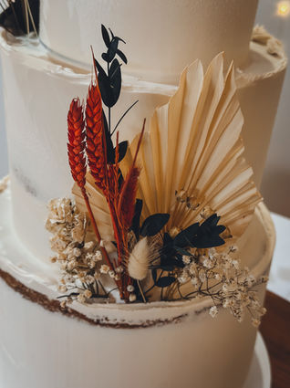 Four-tier semi-naked wedding cake decorated with dried flowers in warm tones, set beneath a copper hoop at The Matara Centre.