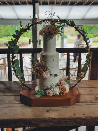 Three-tier semi-naked wedding cake with dried and fresh florals, set inside a floral hoop on a wooden stand at Stone Barn.