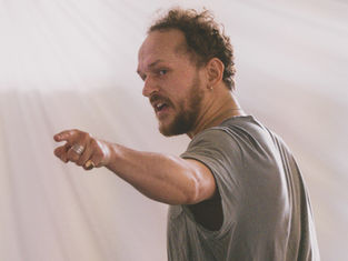An actor in a studio practicing a monologue with his hand raised and open mouth.
