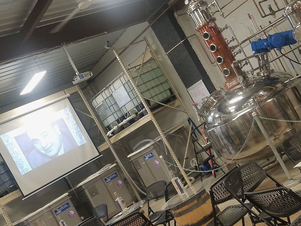 photo of tables and chairs in front of a movie screen next to a still i a distillery
