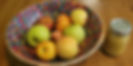 Large wood salad bowl painted with flowers on the inside; 8 green and red apples are in the bowl. The bowl is on a wood table and a mason jar of homemade applesauce is next to the bowl