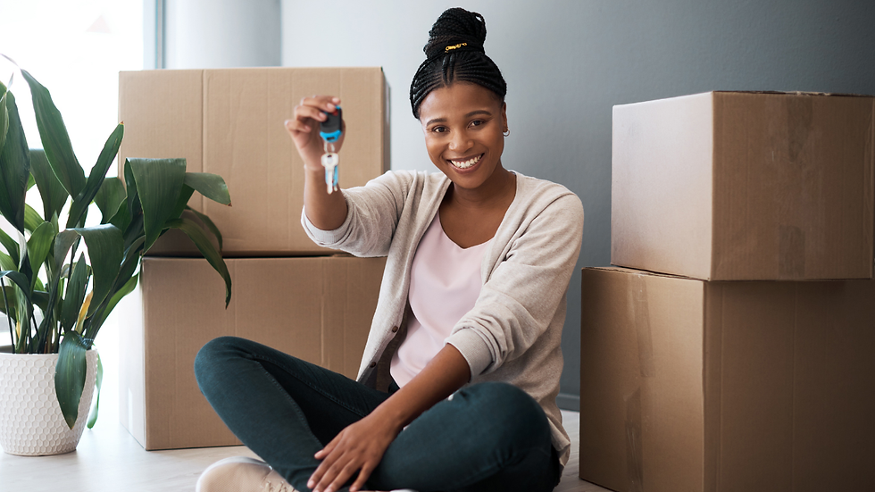 A black woman holding a set of house keys in the air while smiling and sitting in front of moving boxes.