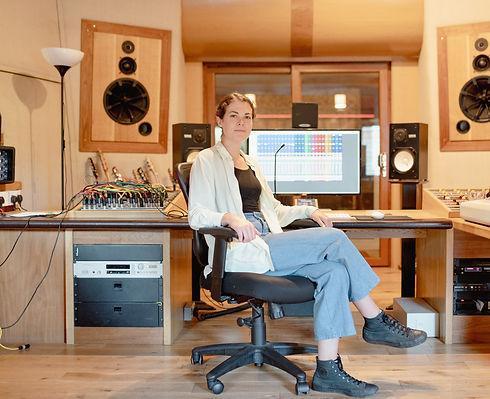 joy stacey is sat on a black office chair in a recording studio with yamaha speakers, and pro tools on the screen