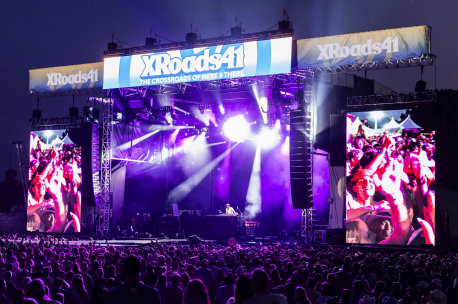 Crowd watches a bright purple concert stage with screens, DJ booth, and XRoads41 banner at an outdoor night festival