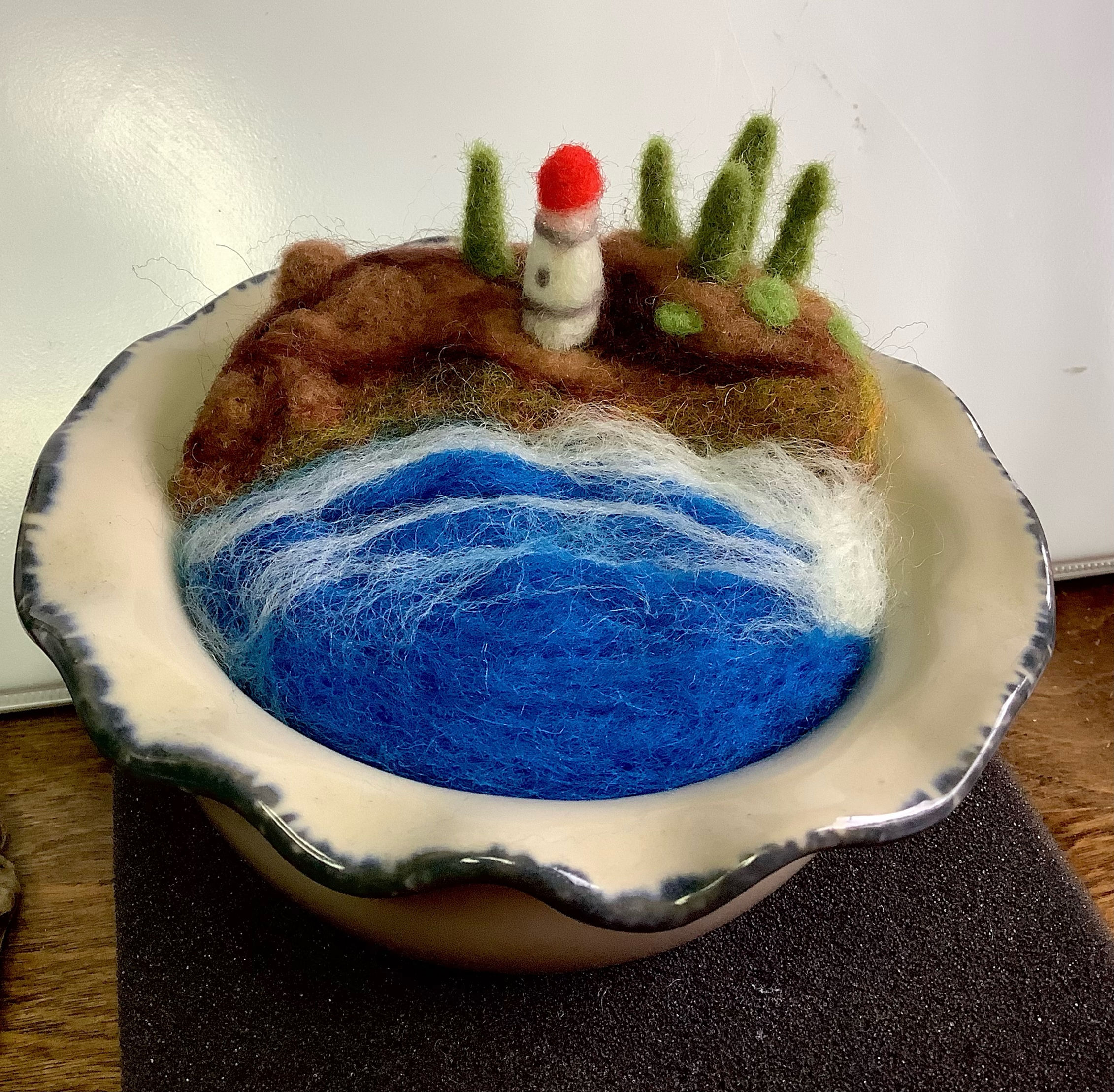Whimsical felted ocean scene with beach lighthouse and trees in ceramic bowl
