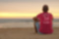 Man sitting on the beach wearing an organic spiced coral red Be like a palm tree T-shirt from Ninefoot