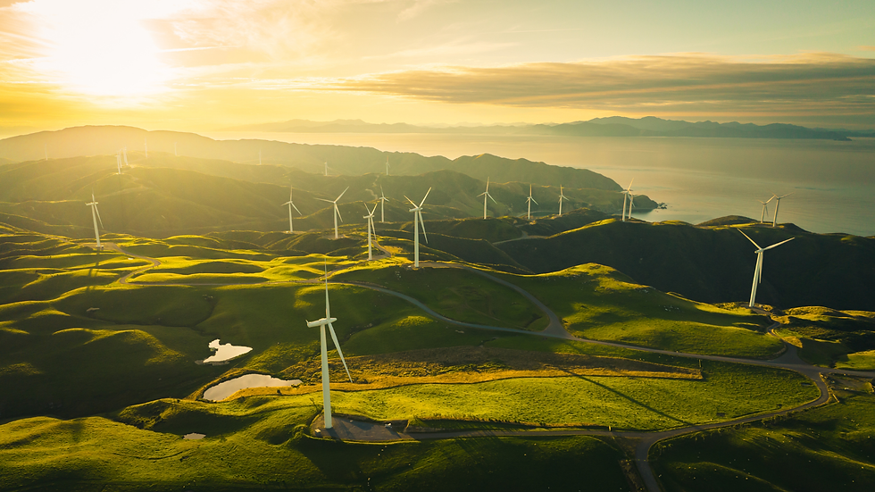 Wind turbines sit atop green hills under a golden sunrise, overlooking a calm sea and mountains in the background, evoking a serene mood.
