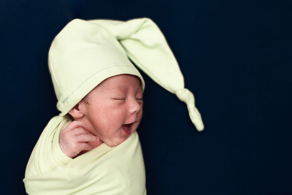 紺色のベロアのシーツの上に寝ている、淡いグリーンのおくるみと帽子を身に纏った、生まれたての男の子が寝ながらあくびをしているニューボーンフォト