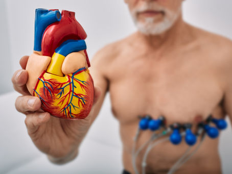 Senior man holding a heart replica with wires attached to his chest near his heart