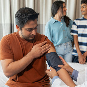  An Australian dad getting his blood pressure checked by a doctor while his family looks on, representing the importance of regular health checks and self-maintenance for dads.