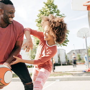 Dad playing basketball and laughing with his daughter, creating fun family memories together.