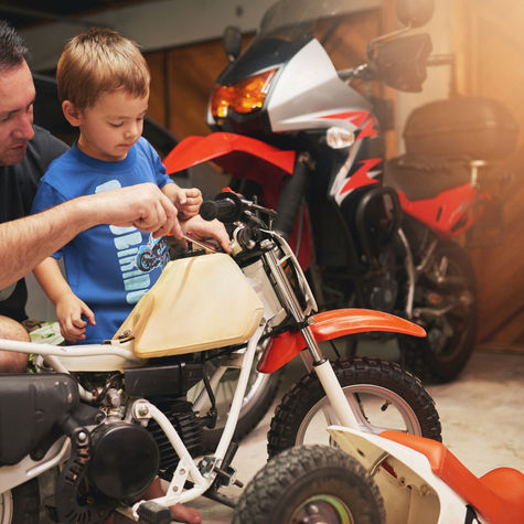 An Australian dad and his young son working together on a small motorbike in the garage, symbolising dads taking time to check in and maintain their own wellbeing during Dad MOT Month.