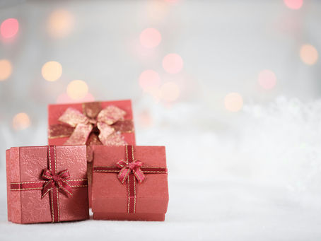 Three wrapped Christmas gifts on a white foreground with lights in the distance in the background.
