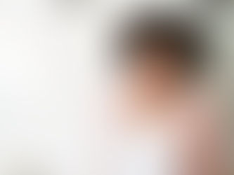 A young professional wearing a white bloue and pale pink blazer smiling, stands in front of a blurred background of a white board.