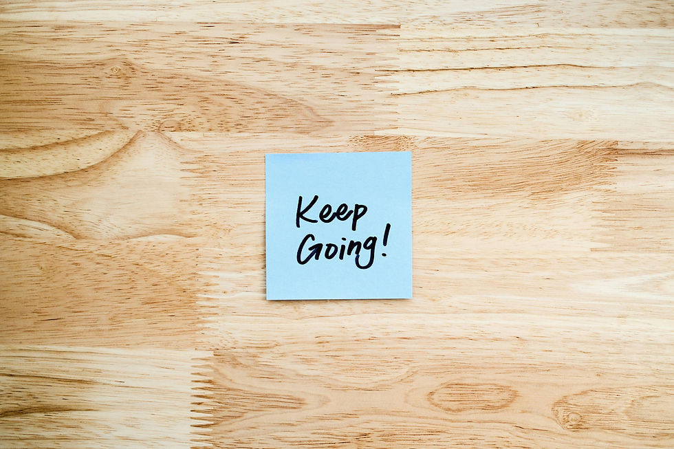 A blue sticky note reads "Keep Going" on a brown woodgrained surface.