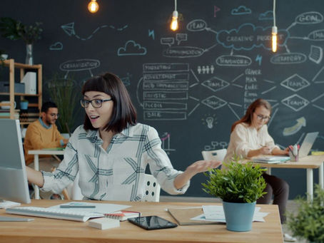 Three coworkers at individual desks, with the coworker front and center, looking excitedly at the computer.