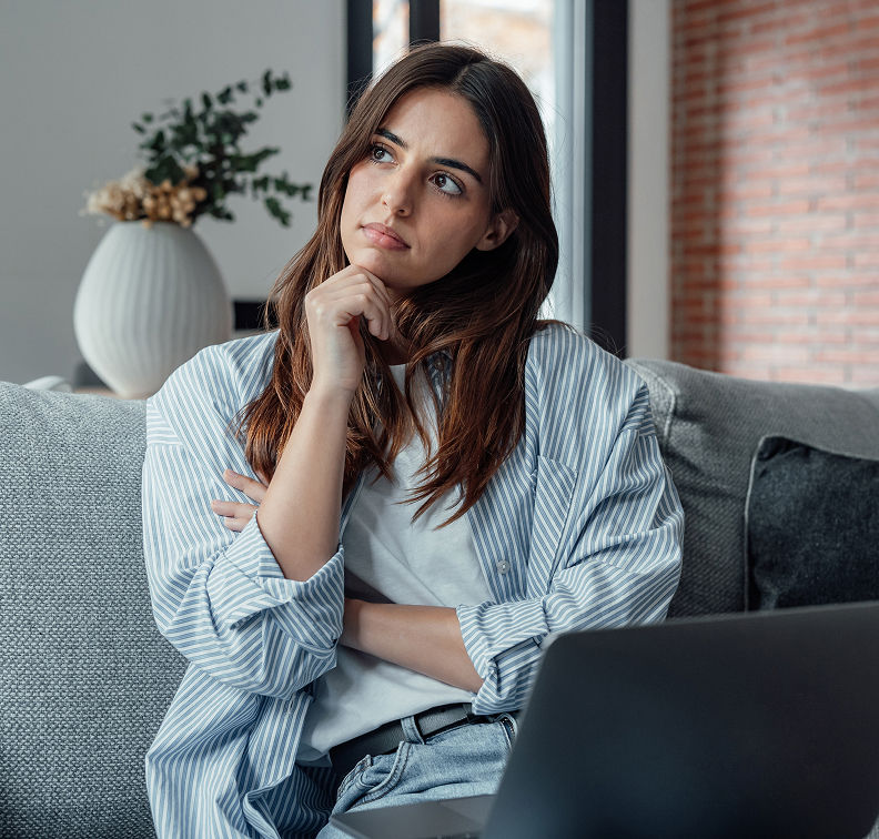 Young woman thinking at home with laptop (life transitions)