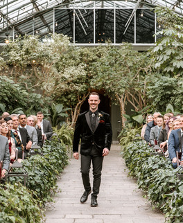 Groom walking down the aisle surrounded by lush greenery at the Planterra Conservatory.