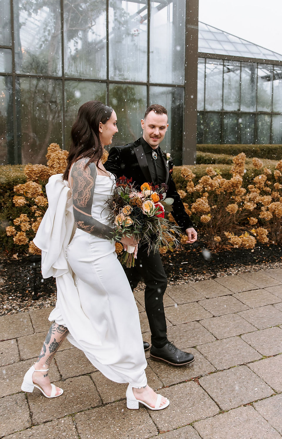 Bride and groom walking in the snow outside the Planterra Conservatory in Michigan.
