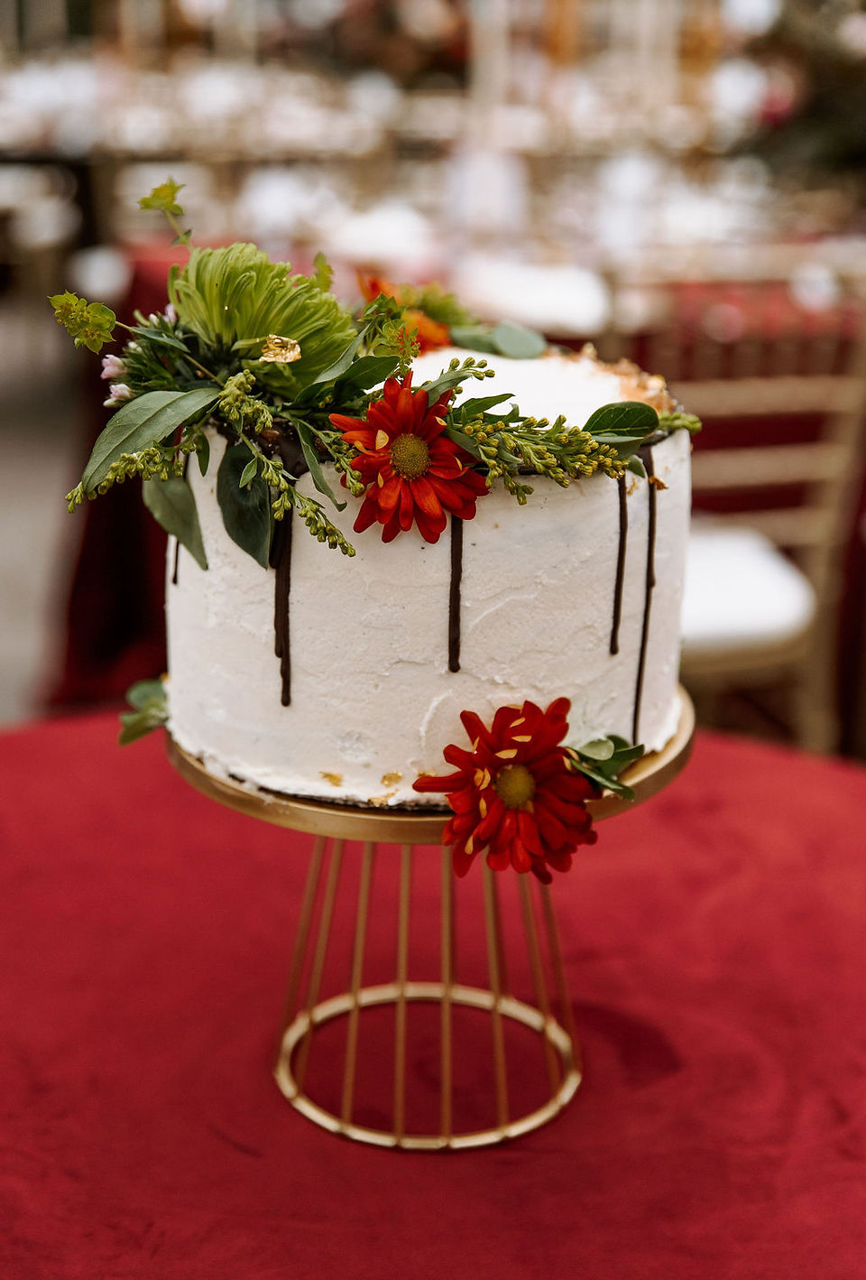 One-tier white wedding cake with red flowers and dripping chocolate sauce.