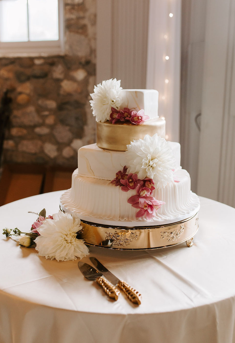 Four tier white wedding cake with gold and flowers.