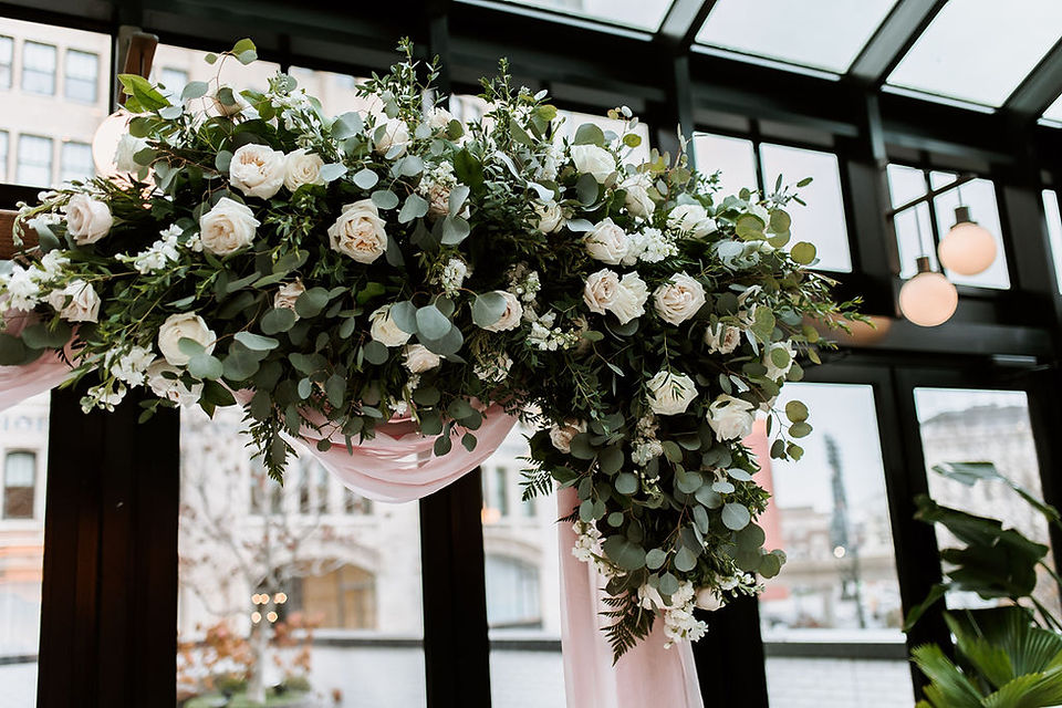 Elegant wedding ceremony arch floral spray with white and pink roses and greenery.