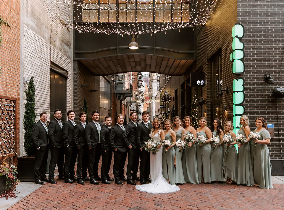 Bride and groom with their wedding party smiling outside the Shinola Hotel in Detroit.