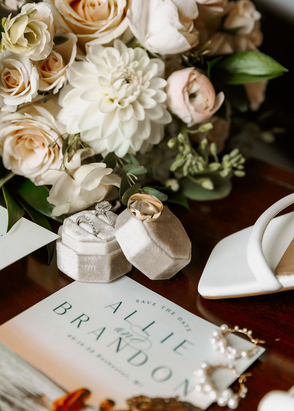 A close up shot of the bride and groom's wedding rings, the bride's strappy white heels and bouquet. 