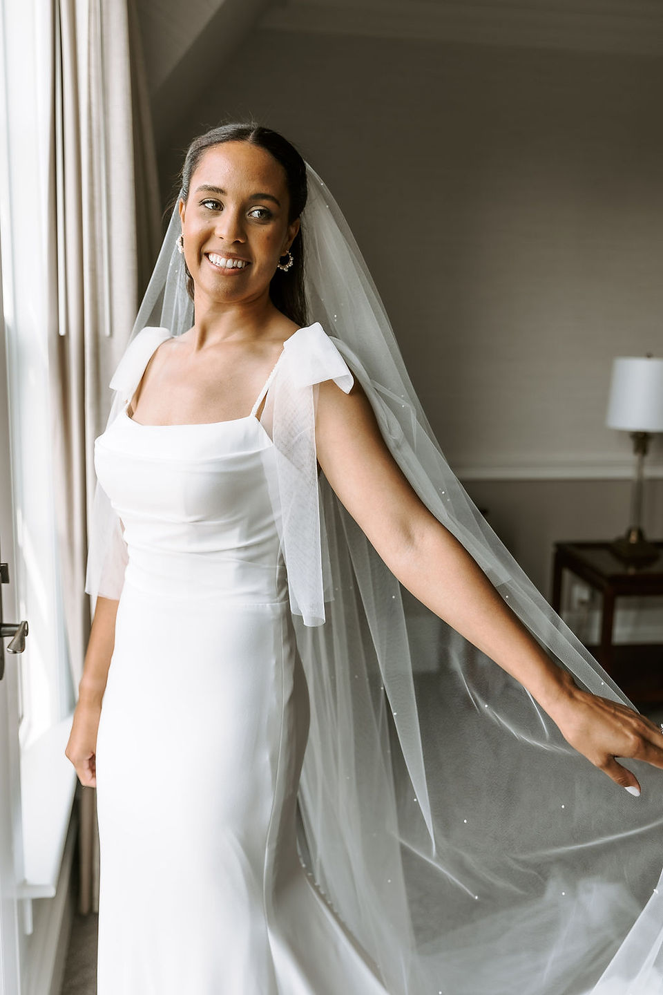 Elegant bridal portrait standing in front of a big window with natural light pouring in.