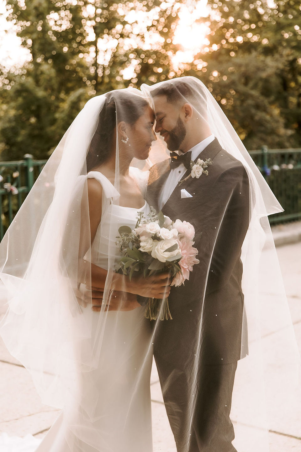 Romantic ethereal portrait of the bride and groom looking into each other's eyes under the veil in golden hour light.