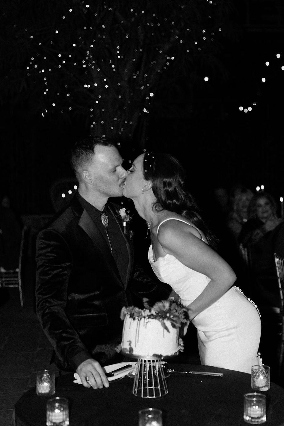 Black and white image of bride and groom kissing after eating a slice of wedding cake.