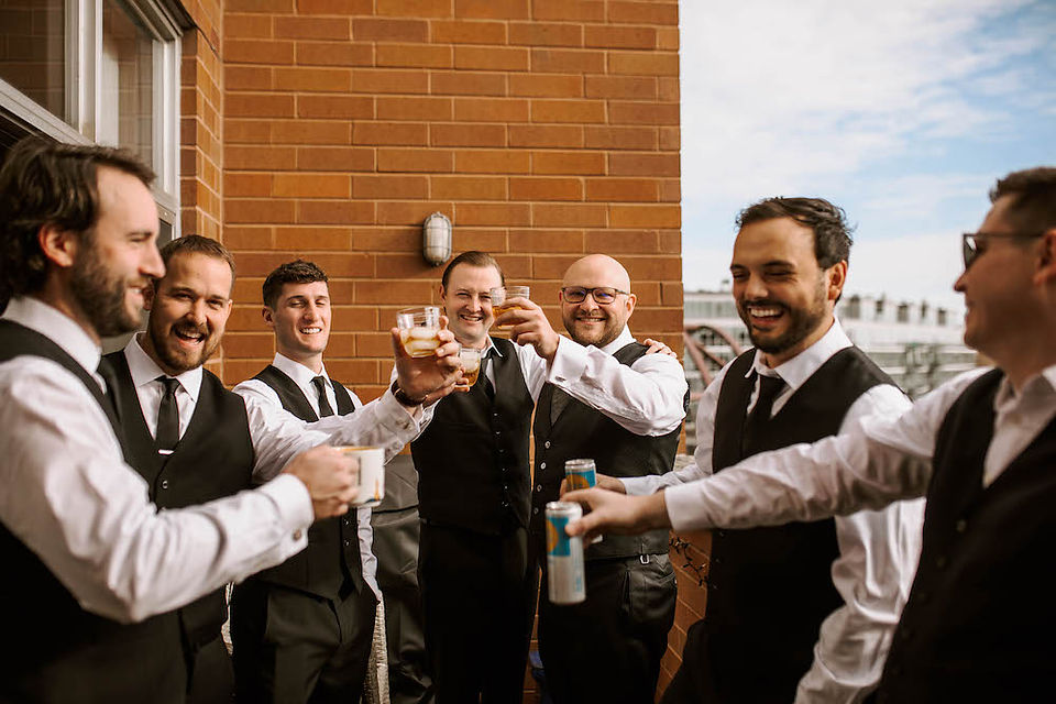 Groom and groomsmen on a balcony clinking their glasses together after a toast. 