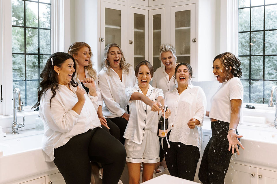 Bride and bridesmaid champagne spray in white and black pajamas.