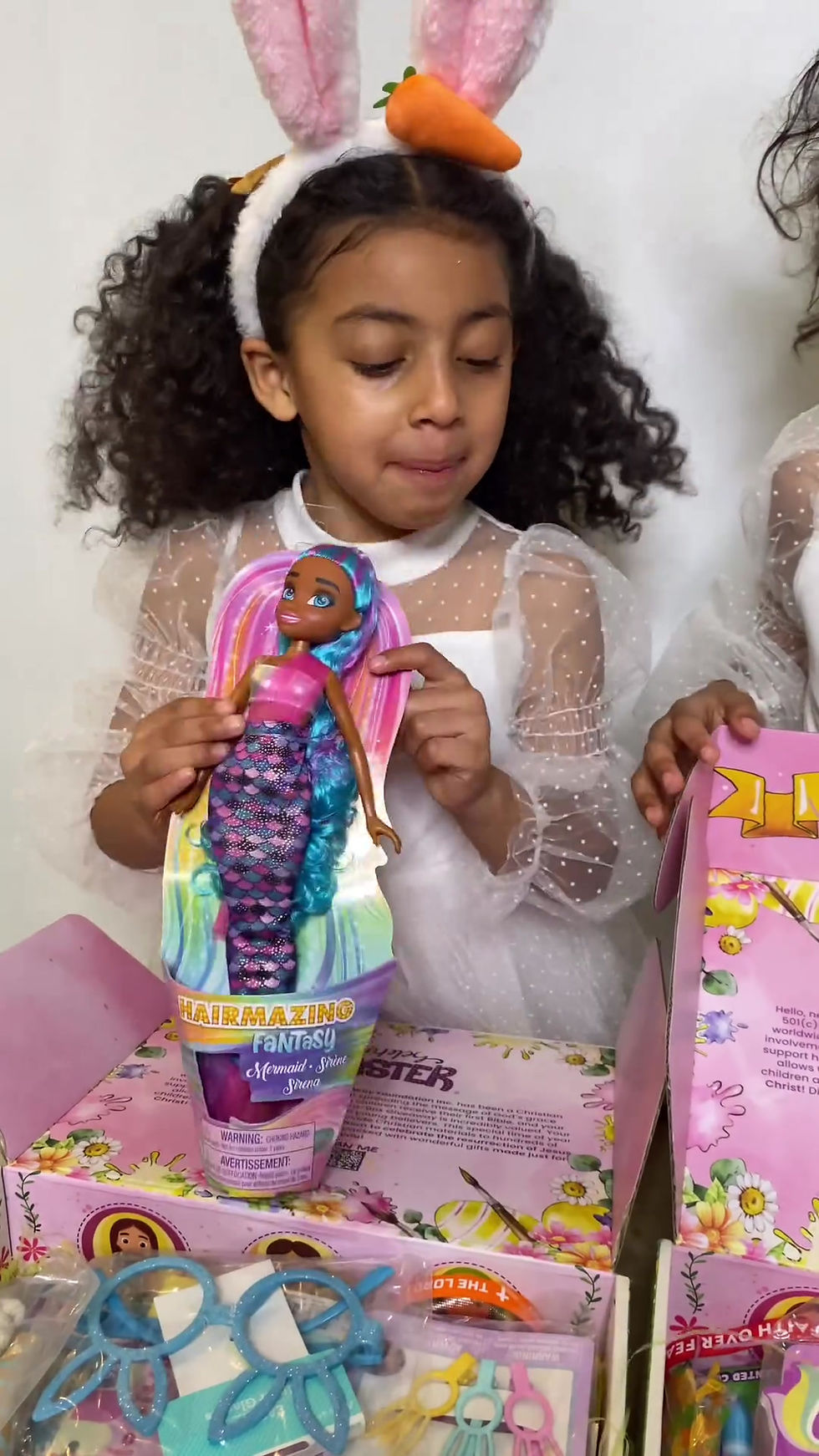 Two young sisters opening the Easter-in-a-Box together, enjoying Christian storybooks, Bible, toys, and faith-based activity