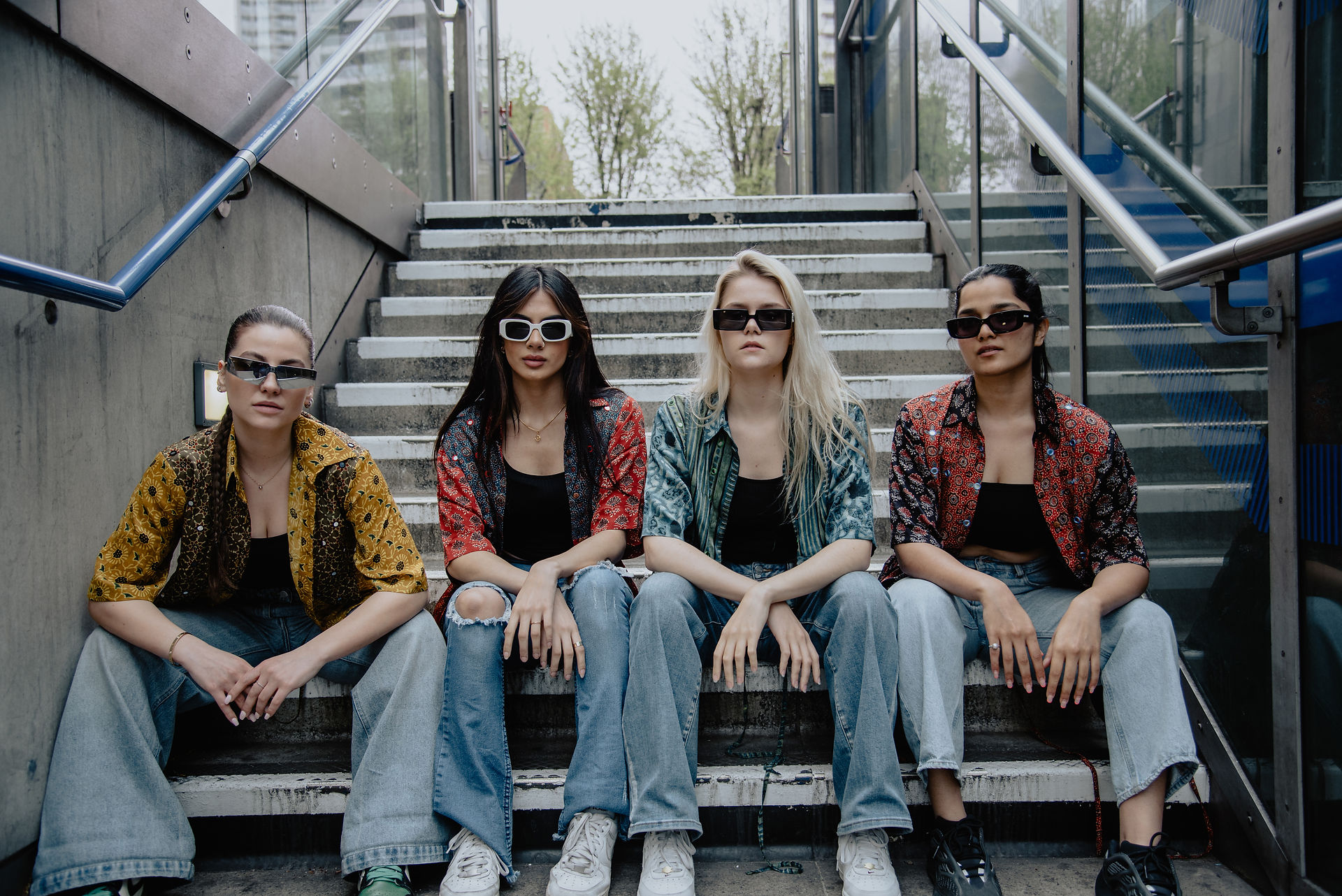 four models in textile jackets and denim jeans sitting on a staircase