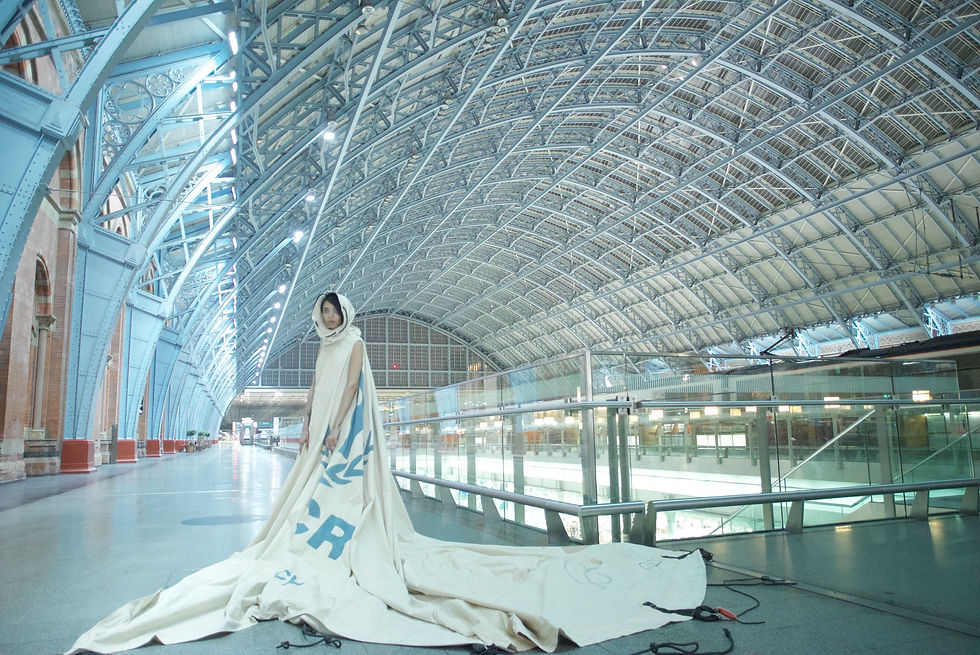 A woman dressed in a donated UNHCR tent which once housed a family at a refugee camp. This dress is part of the project ‘Dress For Our Time’. The woman is standing in London’s St Pancras Station, 2015. Photo by David Betteridge.