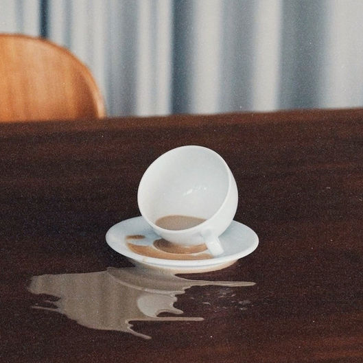 Xícara de café virada sobre a mesa, com o café derramado