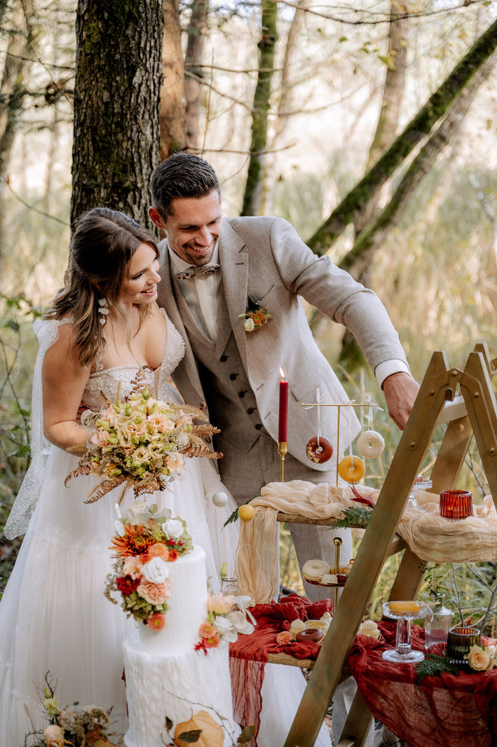 Braut und Bräutigam lachen liebevoll bei ihrer Hochzeit im Freien, umgeben von natürlichen Dekorationen.