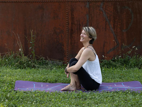 Martina Sailer sitzt lächelnd im Meditatisonsitz auf einer Yogamatte auf einer grünen Wiese