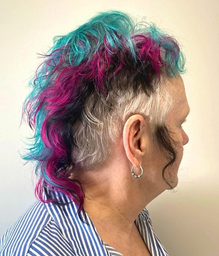 A finished hair client who has a long mullet-mohawk, with layers of teal, magenta, and black hair.