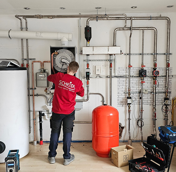 Installateur arbeitet an Heizungsanlage mit Rohren, Pufferspeicher und Steuerungseinheit i